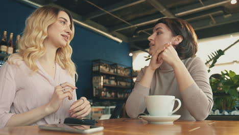 Female-Friends-With-Face-Mask-Talking-In-A-Coffee-Shop