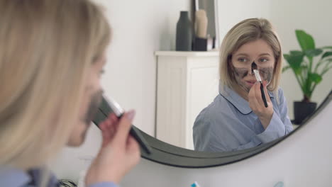 Frau,-Die-Gesichtsmaske-Anwendet,-Die-Zum-Spiegel-Schaut