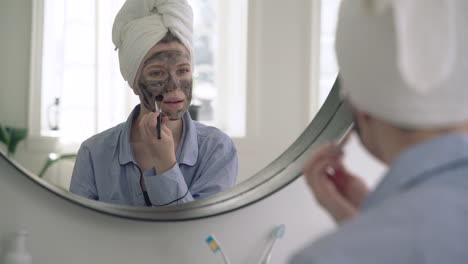 Frau,-Die-Eine-Gesichtsmaske-Anwendet-Und-In-Den-Spiegel-Schaut-1