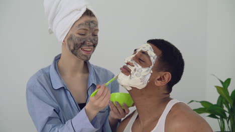 Female-With-Facial-Mask-Applying-Scrub-To-A-Handsome-Black-Male