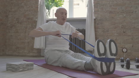 Old-Man-Using-A-Stretching-Band-And-Exercising-On-Yoga-Mat-At-Home