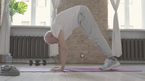 Old-Male-Stretching-And-Exercising-On-Yoga-Mat-At-Home