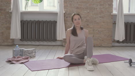 Alte-Frau-Bindet-Ihre-Schnürsenkel,-Die-Zu-Hause-Auf-Yogamatte-Sitzen