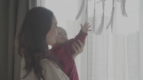 Mom-With-Her-Cute-Baby-In-Her-Arms-Looking-Out-The-Window