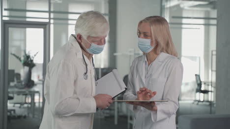 A-Pair-Of-Doctors-With-Masks-Converse-While-Looking-At-Results-On-A-Tablet