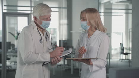 A-Pair-Of-Doctors-With-Masks-Converse-While-Looking-At-Results-On-A-Tablet-1