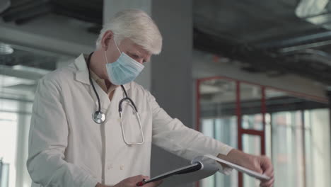 A-Grey-Haired,-Middle-Aged-Doctor-In-A-Facemask-Takes-Notes-In-A-Notebook-1