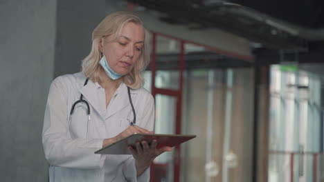 A-Blonde,-Middle-Aged-Female-Doctor-Consults-Data-On-A-Tablet