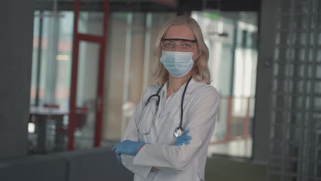 A-Blonde,-Middle-Aged-Female-Doctor-In-A-Facemask-Looks-Directly-At-The-Camera-With-Crossed-Arms