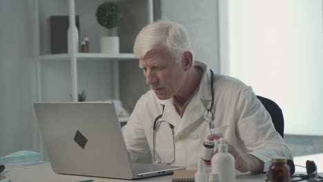 A-Grey-Haired,-Middle-Aged-Doctor-Consults-On-His-Laptop-The-Composition-Of-A-Medicine