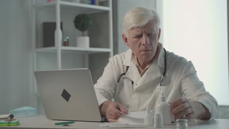 A-Grey-Haired,-Middle-Aged-Doctor-Consults-On-A-Notebook-The-Composition-Of-A-Medicine