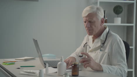 A-Grey-Haired,-Middle-Aged-Doctor-Consults-On-His-Laptop-The-Composition-Of-A-Medicine-2