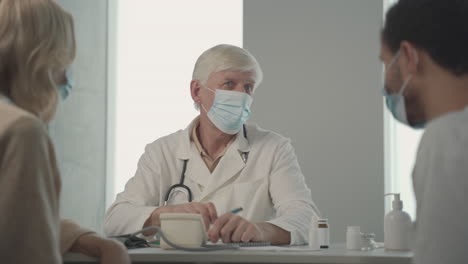 Ein-Grauhaariger-Arzt-Mittleren-Alters-Mit-Gesichtsmaske,-Der-Einem-Jungen-Schwarzen-Mann-Fragen-Stellt-1