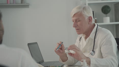 A-Grey-Haired,-Middle-Aged-Doctor-Talking-About-Tablets-To-Some-Patients