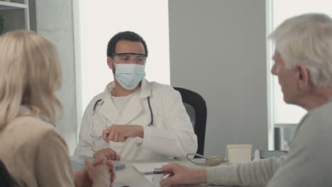 A-Young-Black-Doctor-In-A-Facemask-Listening-To-A-Ederly-Couple-1