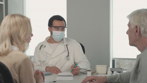 A-Young-Black-Doctor-In-A-Facemask-Talking-To-A-Ederly-Couple