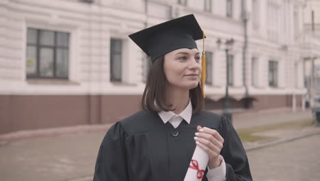 Pretty-Girl-Graduate-Student-In-Gown-And-Cap-With-Diploma-Looking-At-The-Camera-And-Smiling