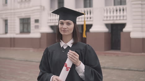 Pretty-Girl-Graduate-Student-In-Gown-And-Cap-With-Diploma-Looking-At-The-Camera-And-Smiling-1