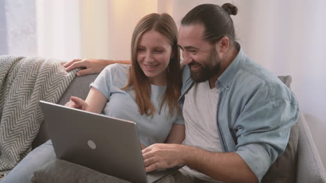 A-Happy-Couple-Have-A-Relaxed-Conversation-Sitting-On-The-Sofa-And-Looking-At-The-Laptop