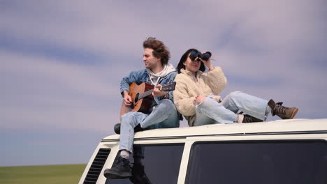 A-Young-Boy-Plays-The-Guitar-And-A-Young-Girl-Looks-Around-With-A-Pair-Of-Binoculars-On-The-Roof-Of-A-Caravan