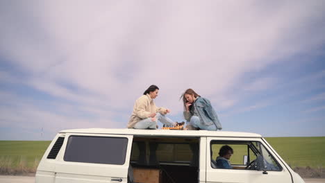 Two-Young-Girls-Play-Chess-On-The-Roof-Of-A-Caravan-On-A-Road-Lost-In-The-Middle-Of-The-Countryside