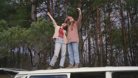 Zwei-Junge-Freundinnen-Machen-Ein-Selfie-Miteinander-Auf-Dem-Dach-Eines-Wohnwagens-Mitten-Im-Wald