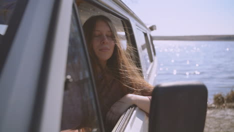 A-Young-Long-Haired-Red-Haired-Girl-Sitting-In-A-Caravan-By-A-Lake-Looks-At-The-Camera