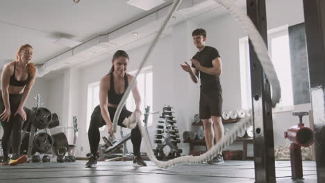 An-Athletic-Woman-Works-With-Battling-Ropes-While-Gym-Buddies-Support-Her
