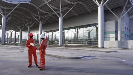 Bauarbeiter-In-Orangefarbenen-Uniformen-Und-Helmen-Schauen-Sich-Gemeinsam-Die-Pläne-An