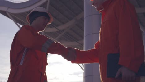 Closeup-View-Of-Two-Construction-Workers-In-Orange-Uniform-And-Hardhats-Shaking-Hands-At-The-Bulding-Object-1