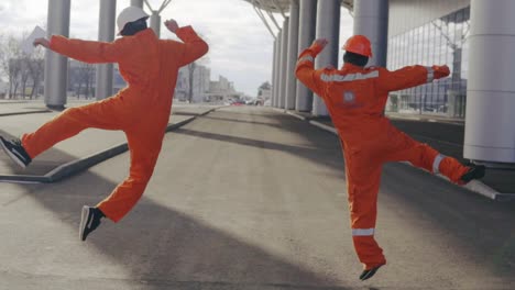 Two-Happy-Construction-Workers-In-Orange-Uniform-And-Helmets-Walking-And-Jumping-Together