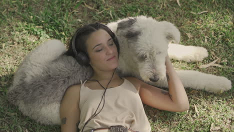 Young-Woman-With-Headphones-Pets-A-Big-Dog-Lying-On-The-Grass