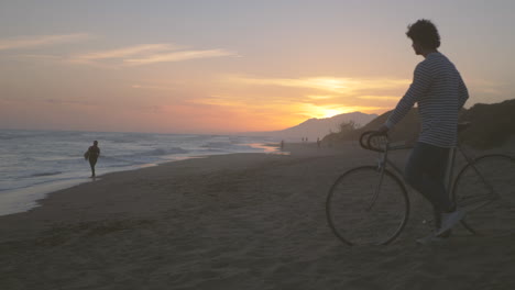 Hombre-Con-Bicicleta-En-La-Playa,-Hermoso-Paisaje-De-Puesta-De-Sol