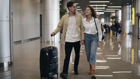 Front-View-Of-Smiling-Couple-Walking-Together-In-Airport-Going-On-Vacation-Or-Trip