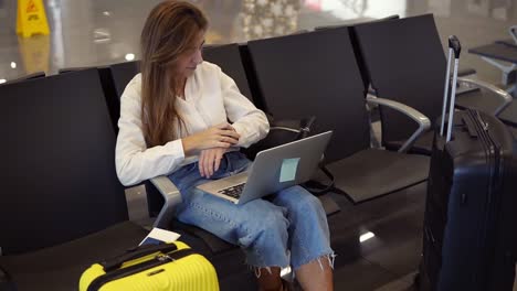 Langhaarige-Moderne-Frau-Sitzt-In-Der-Abflughalle-Und-Nutzt-Laptop-Für-Die-Arbeit-Am-Flughafen