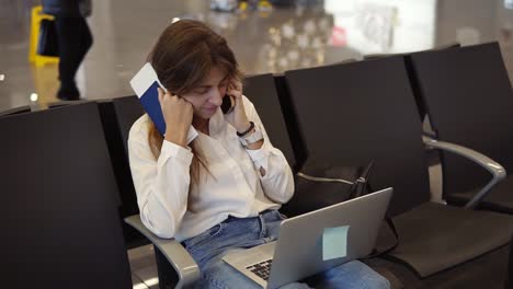 Stylish,Pretty-Girl-In-White-Shirt-Uses-Phone-And-Laptop-To-Work-At-Airport-While-Waiting-Boarding-At-Departure-Lounge