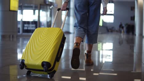 Stylish-Woman-Walk-With-Trolley-Yellow-Case-By-Empty-Airport,-Low-Half-View-Of-Slender-Female-Legs-And-Medium-Wheeled-Bag,-Smooth-Tracking-Shot