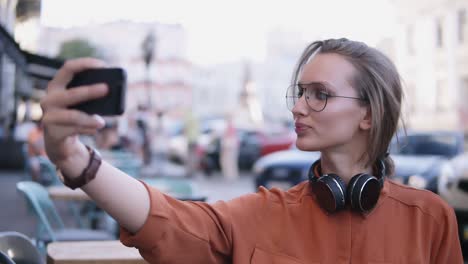 Fröhliche,-Attraktive-Frau-In-Orangefarbenem-Hemd-Und-Sonnenbrille,-Die-Selfie-Auf-Der-Smartphone-Kamera-Macht,-Posiert,-Auf-Der-Straße-Steht