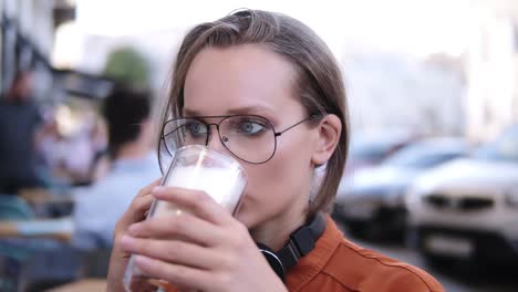 Close-Up-Footage-Of-A-Beautiful-Blonde-Girl-Talking-By-Mobile-While-Drinking-Cappuccino-From-Glass