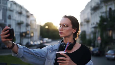 Portrait-Of-Young-Attractive-Woman-In-Sun-Glasses-With-Headphones-On-Neck-Posing-On-The-Camera-In-The-City-Street
