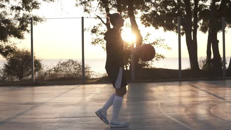 Junge-Basketballspielerin,-Die-Morgens-Am-Basketballplatz-Im-Freien-Vorbeigeht,-Während-Sie-Den-Ball-Hüpft