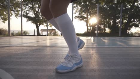 Close-Up-Of-A-Female-Basketball-Player-In-White-Golf-Socks-And-Blue-And-White-Sneakers-Training-Outdoors-On-The-Court,-Bouncing-A-Ball
