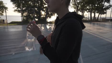 Down-Up-Footage-Of-A-Young-Sporty-Girl-Basketball-Player-Have-A-Rest-After-Training-On-The-Local-Outdoors-Court,-Drinking-A-Water-From-A-Plastic-Bottle