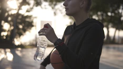 Down-Up-Footage-Of-A-Young-Sporty-Girl-Basketball-Player-Have-A-Rest-After-Training-On-The-Local-Outdoors-Court,-Drinking-A-Water-From-A-Plastic-Bottle-1