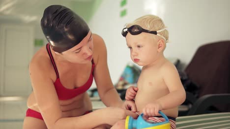 Young-Mother-And-Her-Cute-Little-Blonde-Child-Sitting-By-The-Swimming-Pool-And-Preparing-For-The-Swimming-Lesson