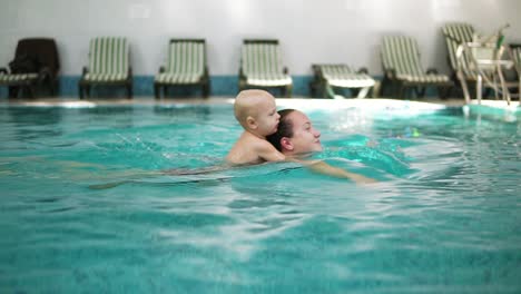 Young-Mother-Is-Swimming-In-The-Pool-Holding-Her-Little-Cute-Toddler-On-Her-Back