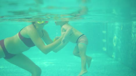 An-Underwater-Shot-Of-Cute-Blonde-Toddler-Swimming-Under-The-Water-Together-With-His-Mother-In-The-Swimming-Pool