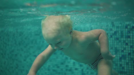 Cute-Blonde-Toddler-Is-Diving-Under-The-Water-In-The-Swimming-Pool-And-Swimming-There-Until-His-Mother-Is-Lifting-Him-From-The-Water