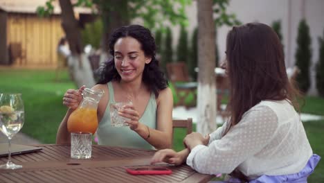 People,-Communication-And-Friendship-Concept-Smiling-Young-Women-Drinking-Orange-Juice-And-Talking-At-Outdoor-Cafe,-Smiling