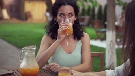 Young-Women-Drinking-Orange-Juice-And-Talking-At-Outdoor-Cafe,-Smiling-Portrait-Of-Brunette-Woman-Drinking-Juice